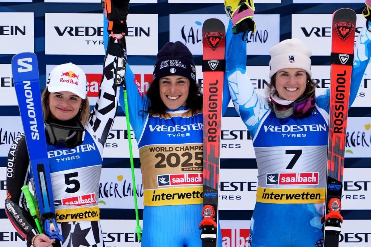La italiana Federica Brignone sonríe en el centro del podio tras ganar el oro en el gigante de los Mundiales de Saalbach 2025. A su izquierda, la neozelandesa Alice Robinson, medalla de plata, y a su derecha, la estadounidense Paula Moltzan, bronce. Las tres esquiadoras levantan sus esquís en señal de celebración frente al fondo con los logotipos del evento y los patrocinadores.